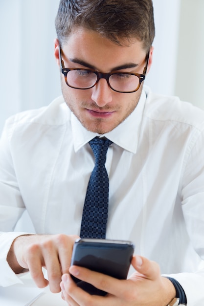 Jovem e bonito trabalhando em seu escritório com telefone celular.