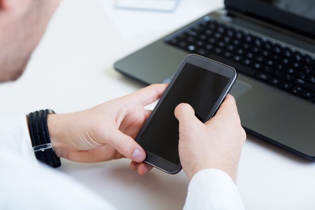 Jovem e bonito trabalhando em seu escritório com telefone celular.