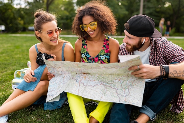 Jovem e feliz companhia de amigos sentados no parque, viajando, olhando no mapa turístico, homens e mulheres se divertindo juntos