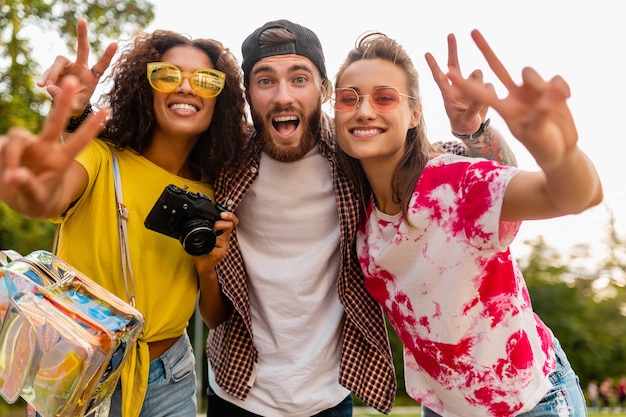 Jovem e feliz companhia de amigos sorridentes e emocionais caminhando no parque com a câmera fotográfica, homens e mulheres se divertindo juntos