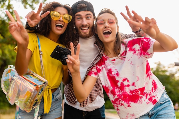 Jovem e feliz companhia de amigos sorridentes e emocionais caminhando no parque com a câmera fotográfica, homens e mulheres se divertindo juntos