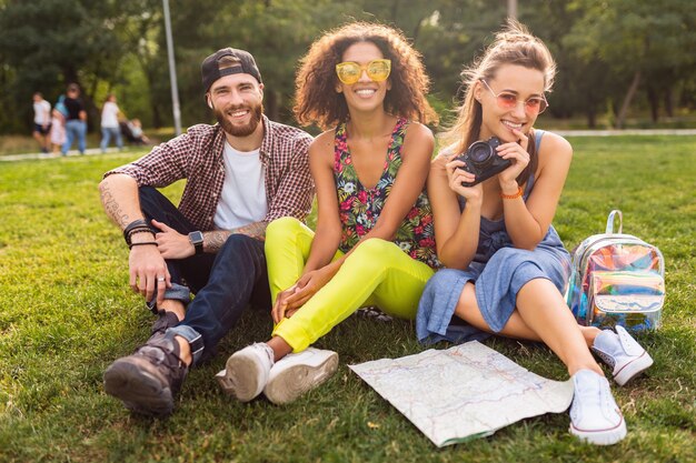 Jovem e feliz companhia de amigos sorridentes sentados no parque, homens e mulheres se divertindo juntos, viajando com a câmera