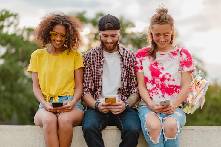 Foto grátis jovem e feliz companhia de amigos sorridentes sentados no parque usando smartphones