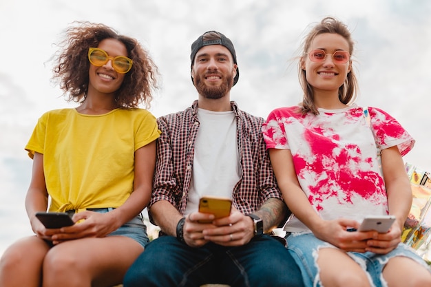 Foto grátis jovem e feliz companhia de amigos sorridentes sentados no parque usando smartphones