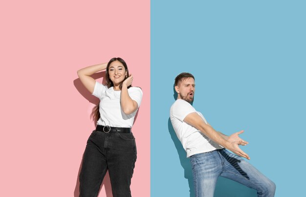 Jovem e feliz homem e mulher em roupas casuais na parede bicolor rosa, azul, dançando