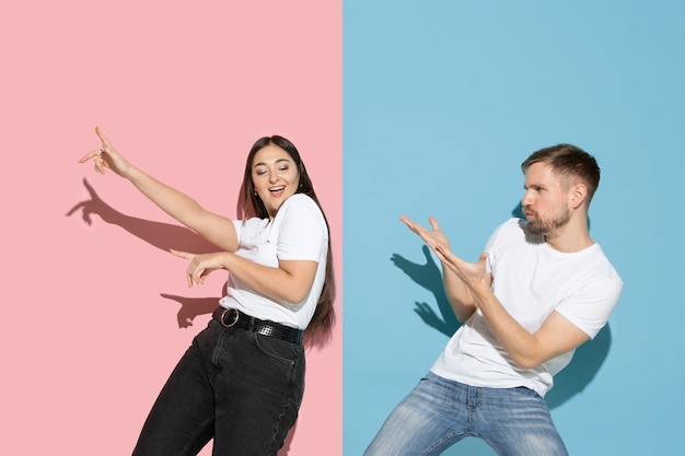 Jovem e feliz homem e mulher em roupas casuais na parede bicolor rosa, azul, dançando