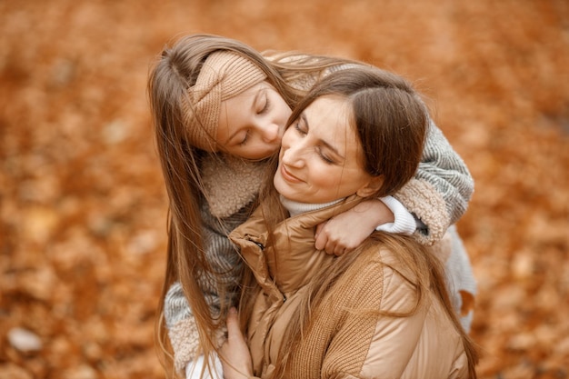 Jovem e garotinha na floresta de outono garotinha beijando sua mãe garota vestindo jaqueta cinza fashion e mulher marrom