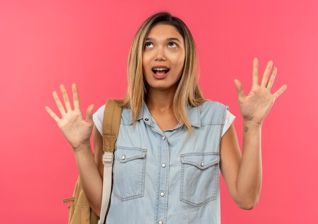 Jovem e linda aluna impressionada com uma bolsa de costas olhando para cima e mostrando as mãos vazias