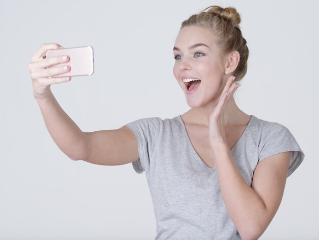 Jovem e linda garota caucasiana faz selfies. Mulher feliz e maravilhosa com o celular nas mãos