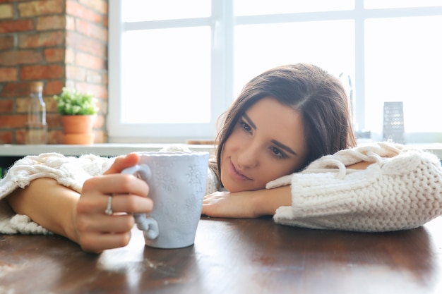 Jovem e linda mulher bebendo uma bebida quente na cozinha