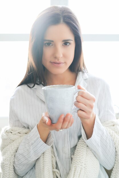 Jovem e linda mulher bebendo uma bebida quente na cozinha