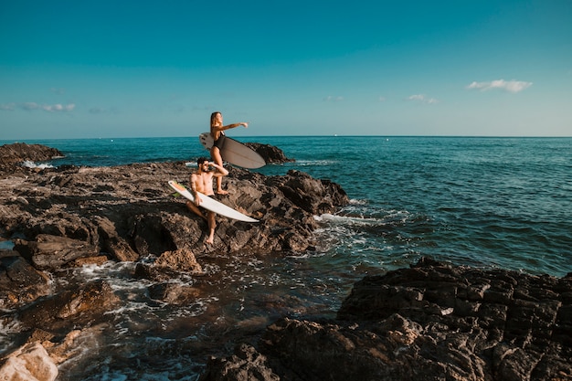 Jovem e mulher apontando para o lado com pranchas de surf na rocha perto do mar