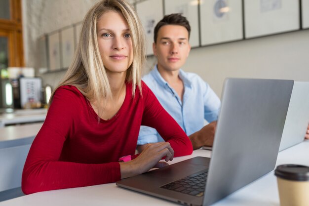 Jovem e mulher trabalhando em um laptop em uma sala de escritório em parceria com espaço aberto,
