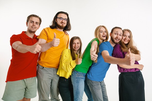 Jovem e mulher vestidos com as cores da bandeira LGBT na parede branca. Modelos caucasianos com camisas brilhantes. Pareçam felizes juntos, sorrindo e se abraçando. Orgulho LGBT, direitos humanos e conceito de escolha.