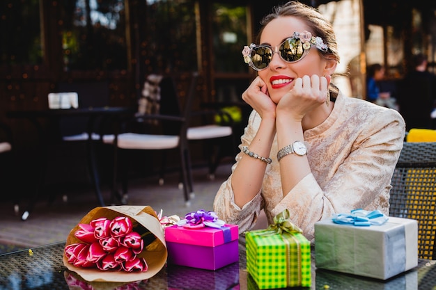 Jovem elegante e bonita na moda óculos de sol sentada no café com presentes