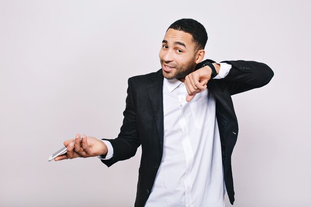 Foto grátis jovem elegante em camisa branca e jaqueta preta se divertindo com o telefone e o relógio. empresário, trabalho, reunião, bom humor, sorrindo