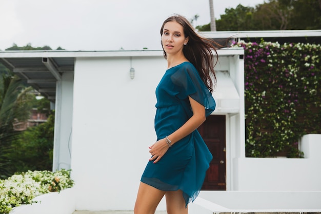 Jovem elegante mulher bonita em um vestido azul, tendência da moda de verão, férias, jardim, terraço de hotel tropical, sorrindo, caminhando