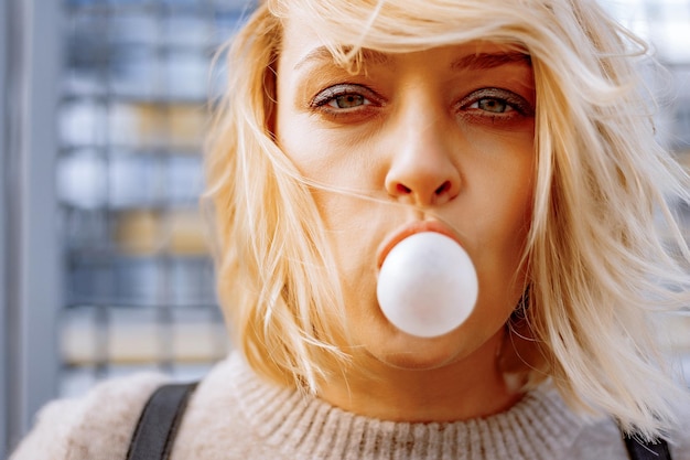 Jovem elegante urbana. Retrato emocional ao ar livre do modelo de mulher ativa. Estilo de vida saudável. Olhar de moda, retrato de hipster ao ar livre. Feche o retrato de uma jovem muito jovem, mascando chiclete.