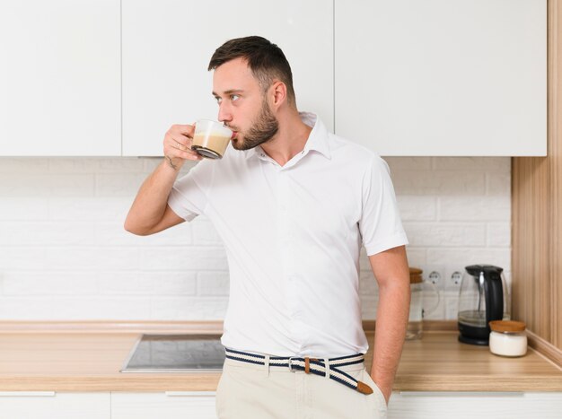 Jovem em camiseta tomando um café na cozinha