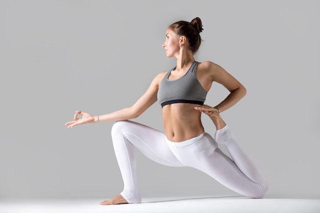 Jovem em Eka Pada Rajakapotasana pose, fundo de estúdio cinza