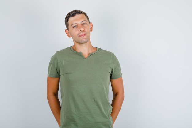 Foto grátis jovem em pé com as mãos nos bolsos traseiros, em camiseta verde exército e aparência elegante. vista frontal.