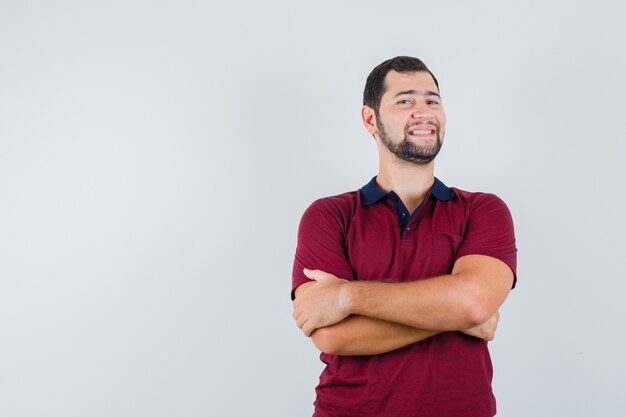 Jovem em pé com os braços cruzados em uma camiseta vermelha e parecendo feliz. vista frontal.