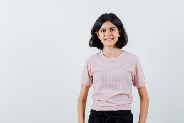 Jovem em pé e posando para a câmera com uma camiseta rosa e calça preta e parecendo feliz