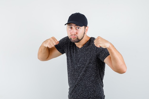 Foto grátis jovem em pé em pose de luta com camiseta e boné e parece poderoso