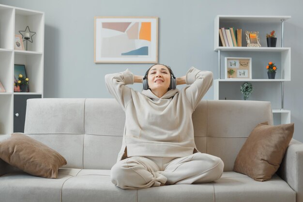 Jovem em roupas casuais com fones de ouvido sentado em um sofá em casa interior feliz e positivo com os olhos fechados relaxando