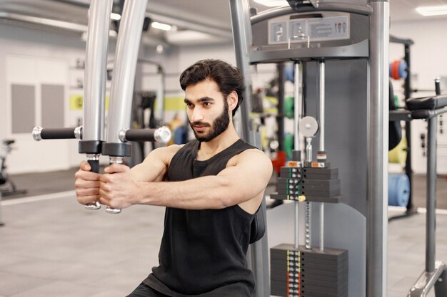 Jovem em roupas esportivas fazendo exercícios em equipamentos especiais na academia