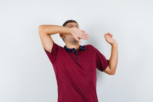 Jovem em t-shirt, bocejando e alongando-se e parecendo relaxado, vista frontal.