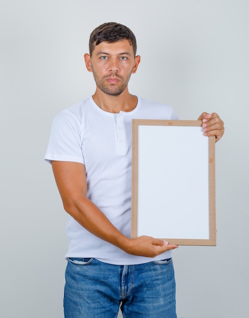 Foto grátis jovem em t-shirt e jeans, segurando um quadro branco, vista frontal.