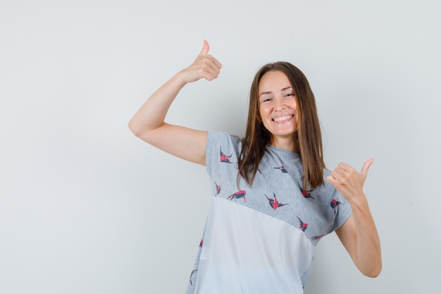 Jovem em t-shirt mostrando os polegares e olhando feliz, vista frontal.