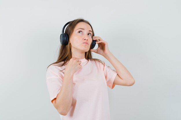 Jovem em t-shirt rosa curtindo música com fones de ouvido e olhando pensativa, vista frontal.