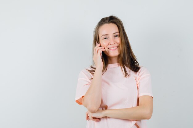 Jovem em t-shirt rosa falando no celular e olhando alegre, vista frontal.