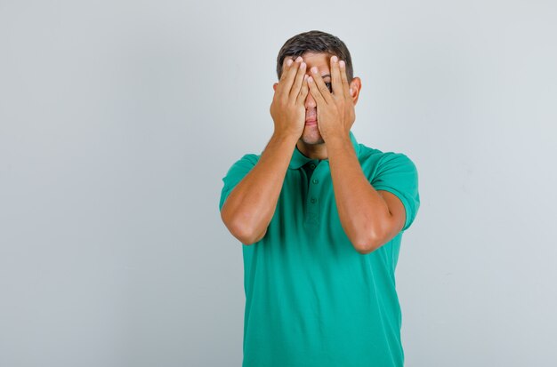 Jovem em t-shirt verde, cobrindo os olhos e olhando desculpe, vista frontal.