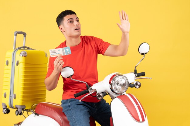 Jovem em uma motocicleta segurando um tíquete e saudando alguém de frente