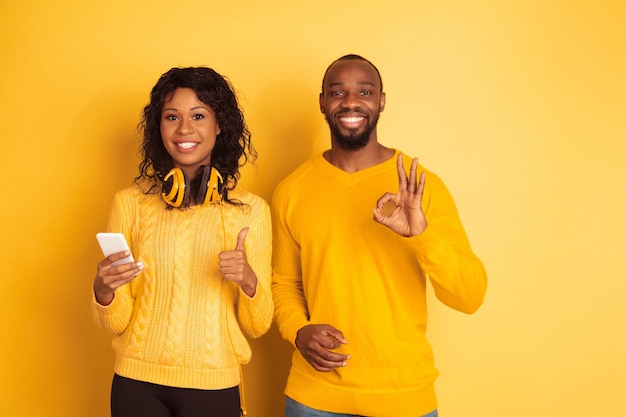 Jovem emocional afro-americano e mulher com roupas casuais brilhantes no espaço amarelo