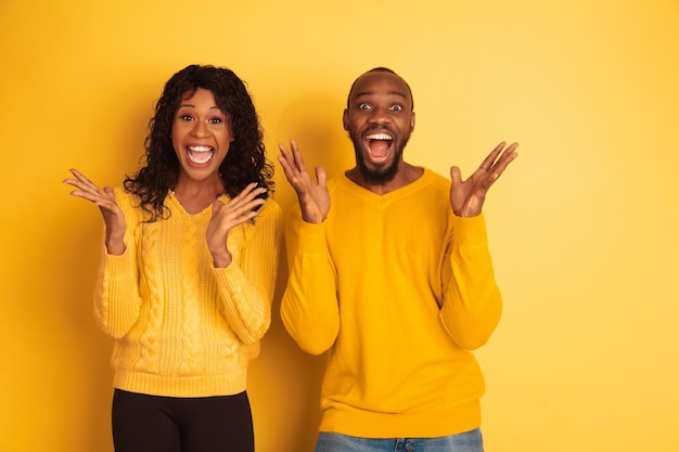 Jovem emocional afro-americano e mulher em roupas casuais brilhantes, posando no espaço amarelo. Casal bonito