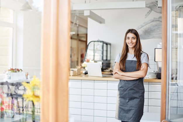 Jovem empresária administrando um pequeno café bem-sucedido em frente à máquina de café com os braços cruzados