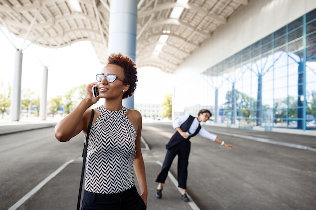 Jovem empresária africana bem sucedida, falando no telefone, sobre o centro de negócios.