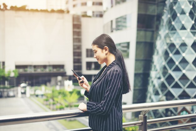 Jovem empresária asiática que usa no smartphone móvel. Profissional jovem feminina na cidade em frente ao grande prédio.