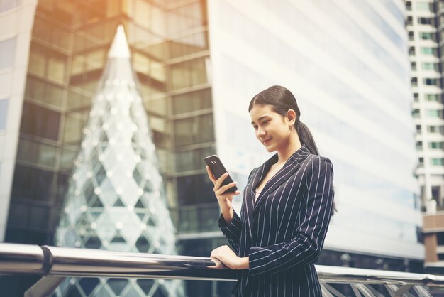 Jovem empresária asiática que usa no smartphone móvel. Profissional jovem feminina na cidade em frente ao grande prédio.