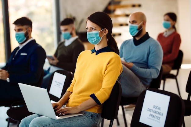 Jovem empresária com máscara facial protetora usando laptop enquanto participava de um evento educacional