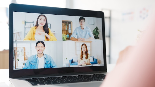 Jovem empresária da Ásia usando laptop fala com um colega sobre o plano de uma reunião de videochamada enquanto trabalha em casa na sala de estar.