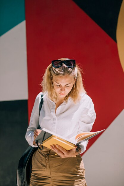 Jovem empresária de pé contra a parede colorida, lendo o livro