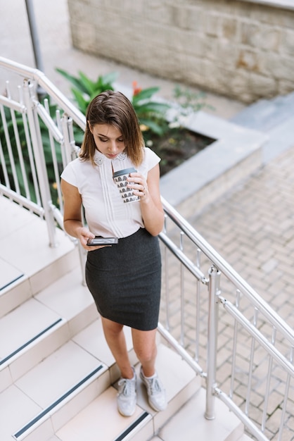 Jovem empresária de pé na escadaria usando smartphone