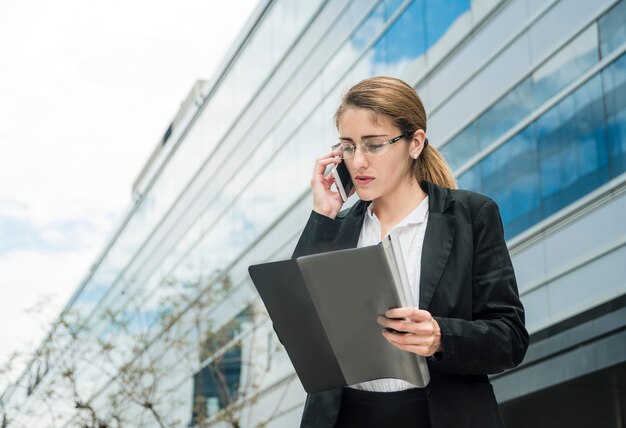 Jovem empresária enquanto fala no celular, olhando para a pasta