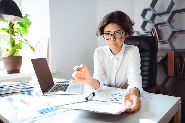 Jovem empresária linda sentada no local de trabalho no escritório.