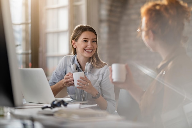 Jovem empresária sorridente e sua colega se comunicando enquanto tomava café no escritório